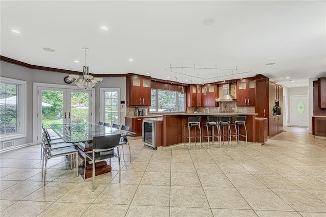 kitchen with a wealth of natural light, hanging light fixtures, wall chimney range hood, tasteful backsplash, and wine cooler