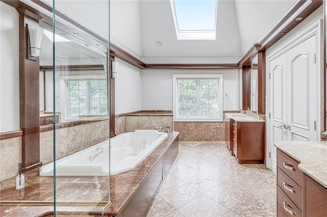 bathroom featuring tiled bath, a skylight, vanity, and high vaulted ceiling