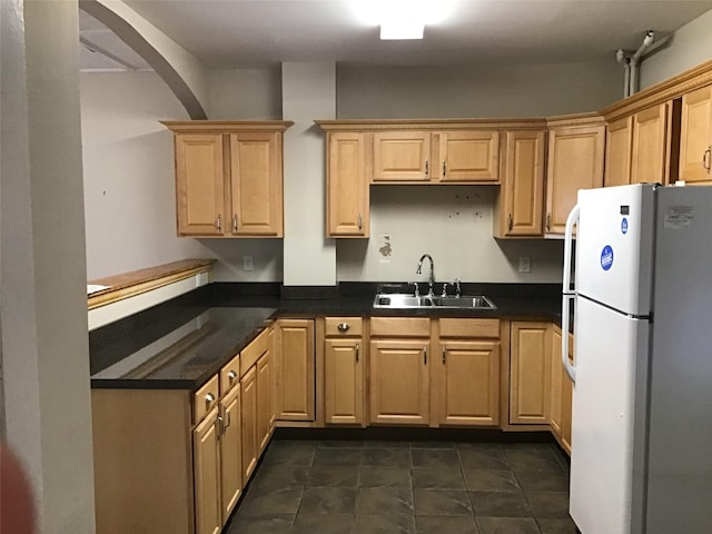 kitchen with dark tile patterned floors, light brown cabinetry, sink, and white fridge