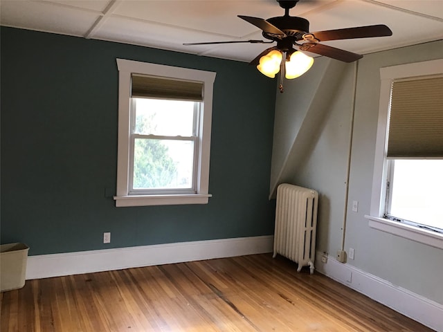 unfurnished room featuring ceiling fan, radiator heating unit, hardwood / wood-style floors, and a drop ceiling