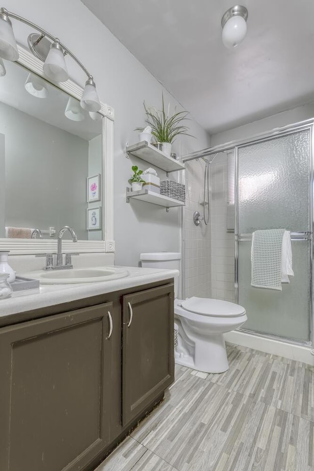 bathroom featuring wood-type flooring, vanity, toilet, and a shower with shower door