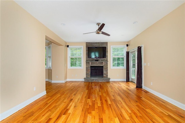 unfurnished living room featuring a stone fireplace, ceiling fan, plenty of natural light, and light hardwood / wood-style floors