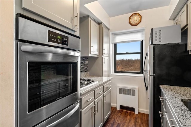 kitchen with dark wood-type flooring, radiator, gray cabinets, light stone counters, and stainless steel appliances