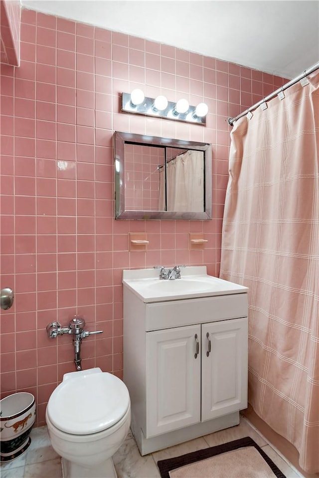 bathroom with curtained shower, tile patterned floors, toilet, vanity, and tile walls