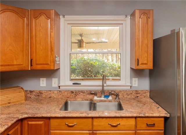 kitchen featuring stainless steel refrigerator, light stone countertops, and sink