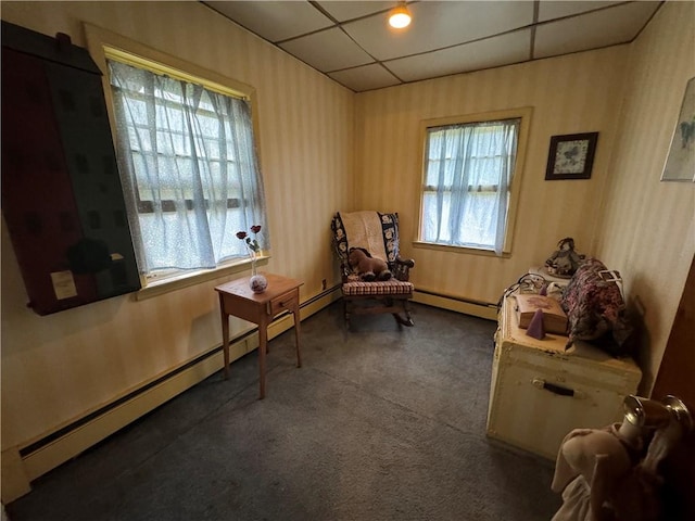 living area featuring dark carpet, plenty of natural light, a drop ceiling, and a baseboard heating unit