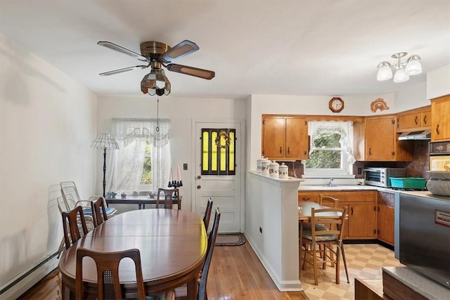 dining area with baseboard heating, light hardwood / wood-style flooring, ceiling fan with notable chandelier, and sink