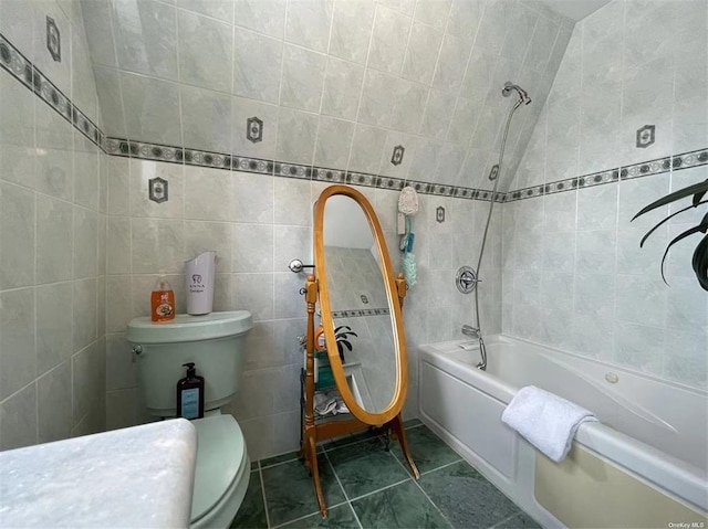 bathroom featuring tiled shower / bath combo, toilet, and tile walls