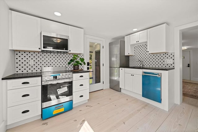 kitchen featuring tasteful backsplash, white cabinetry, light wood-type flooring, and appliances with stainless steel finishes