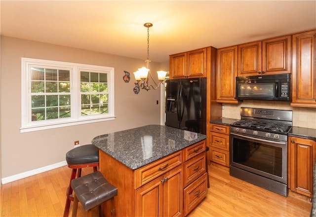 kitchen featuring a breakfast bar, black appliances, light hardwood / wood-style flooring, a chandelier, and a center island