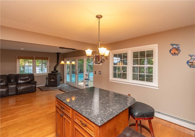 kitchen with a wood stove, a baseboard heating unit, dark stone countertops, a breakfast bar area, and light wood-type flooring