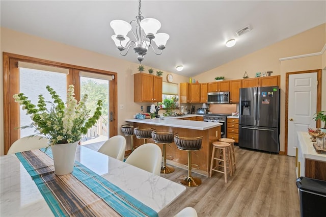 kitchen featuring a chandelier, pendant lighting, lofted ceiling, a kitchen bar, and appliances with stainless steel finishes