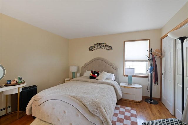 bedroom with light hardwood / wood-style flooring and a baseboard heating unit