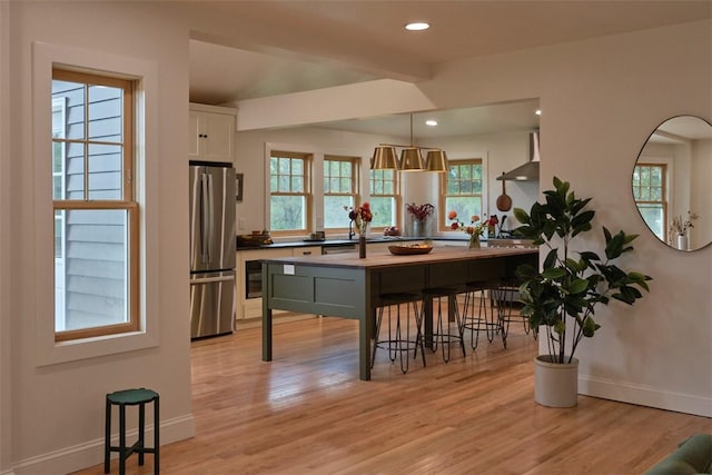 kitchen with a breakfast bar, white cabinets, hanging light fixtures, stainless steel fridge, and light hardwood / wood-style floors