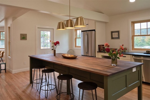 kitchen with a wealth of natural light, light hardwood / wood-style flooring, stainless steel appliances, and decorative light fixtures