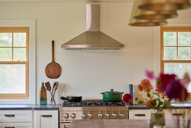 kitchen with white cabinets, stainless steel range, a wealth of natural light, and wall chimney exhaust hood