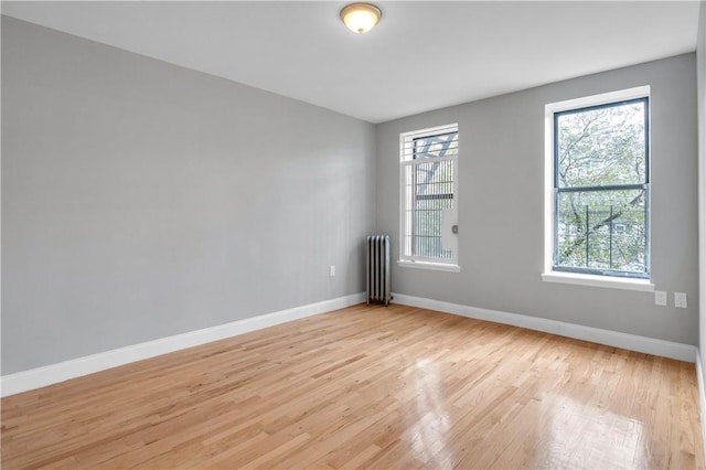 empty room featuring radiator, a wealth of natural light, and light wood-type flooring