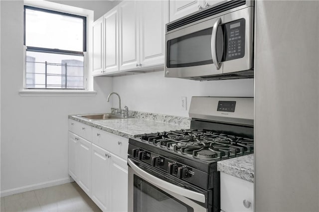 kitchen featuring sink, light stone countertops, appliances with stainless steel finishes, light tile patterned flooring, and white cabinetry