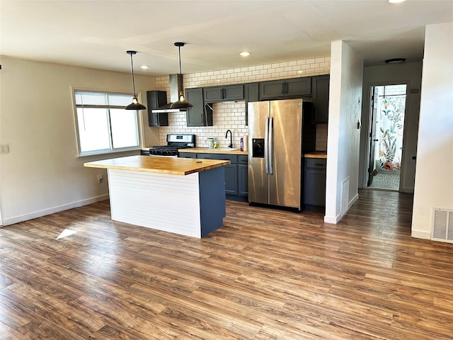 kitchen with visible vents, a sink, stainless steel appliances, wall chimney exhaust hood, and butcher block counters