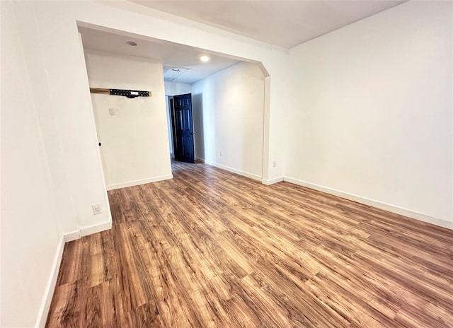 spare room featuring wood finished floors, baseboards, and arched walkways