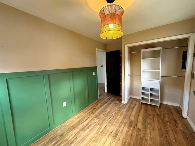 unfurnished bedroom featuring a closet, a wainscoted wall, wood finished floors, and a decorative wall