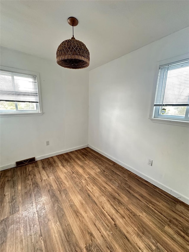 empty room featuring visible vents, wood finished floors, and baseboards