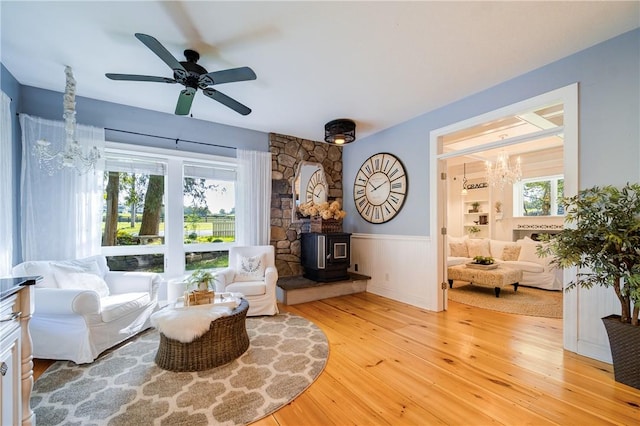 sitting room with ceiling fan with notable chandelier, a wood stove, and light hardwood / wood-style flooring