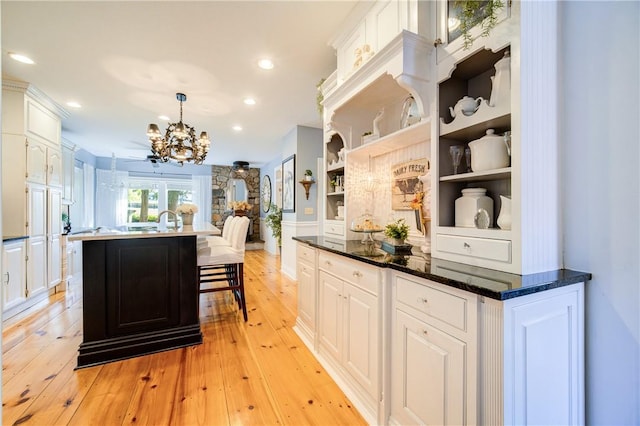 kitchen with white cabinets, hanging light fixtures, an island with sink, a notable chandelier, and light hardwood / wood-style floors