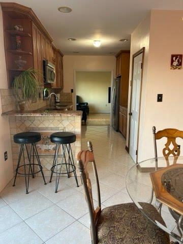 kitchen with kitchen peninsula, a kitchen breakfast bar, decorative backsplash, and stainless steel refrigerator