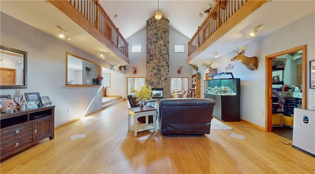 living room with light hardwood / wood-style floors, high vaulted ceiling, and a stone fireplace