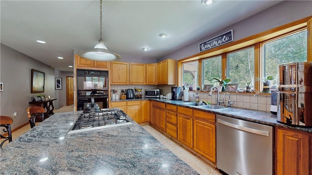 kitchen with sink, hanging light fixtures, dark stone countertops, decorative backsplash, and appliances with stainless steel finishes