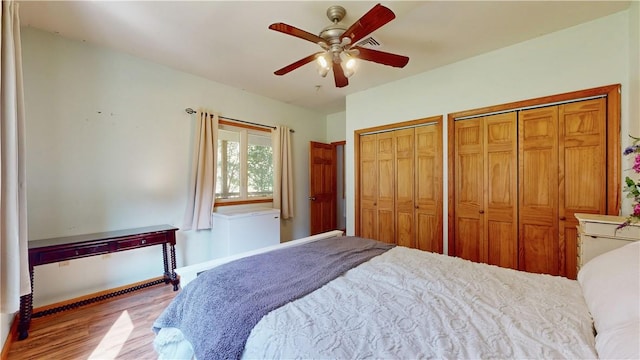 bedroom with ceiling fan, wood-type flooring, and two closets