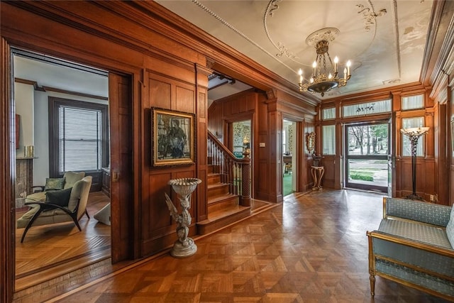 foyer entrance with parquet flooring, ornamental molding, a healthy amount of sunlight, and a notable chandelier