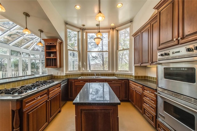 kitchen with appliances with stainless steel finishes, dark stone counters, sink, decorative light fixtures, and a kitchen island