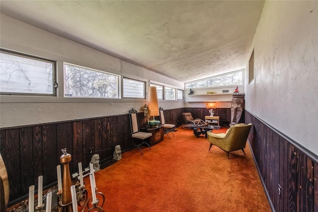 living area featuring carpet flooring, vaulted ceiling, and wooden walls