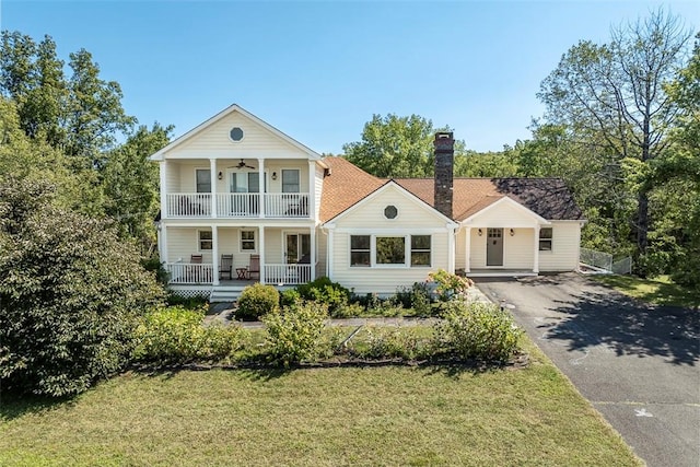 greek revival house with ceiling fan, a porch, a balcony, and a front lawn