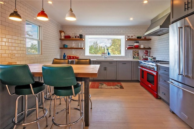 kitchen with sink, hanging light fixtures, wall chimney range hood, wooden counters, and high quality appliances