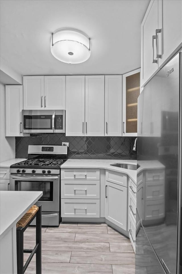 2575 Palisade Ave Unit 2J, Bronx, NY 10463 - kitchen with stainless steel appliances, light countertops, white cabinetry, a sink, and glass insert cabinets