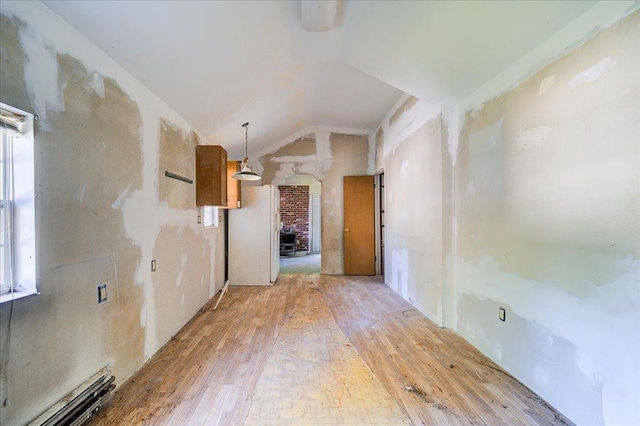 empty room featuring a fireplace, a baseboard radiator, light hardwood / wood-style floors, and lofted ceiling