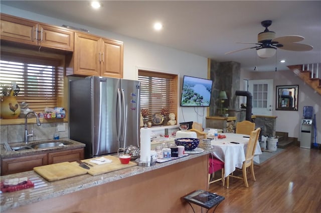 kitchen with stainless steel fridge, dark hardwood / wood-style flooring, ceiling fan, sink, and a wood stove