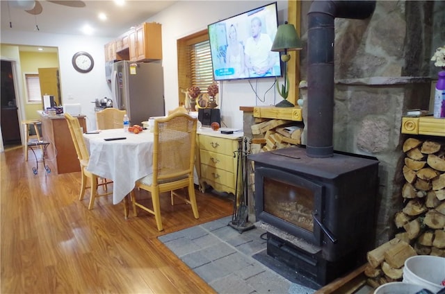 dining space with light hardwood / wood-style floors, a wood stove, and ceiling fan