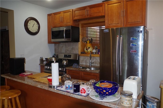 kitchen with kitchen peninsula, stainless steel appliances, light stone counters, and sink