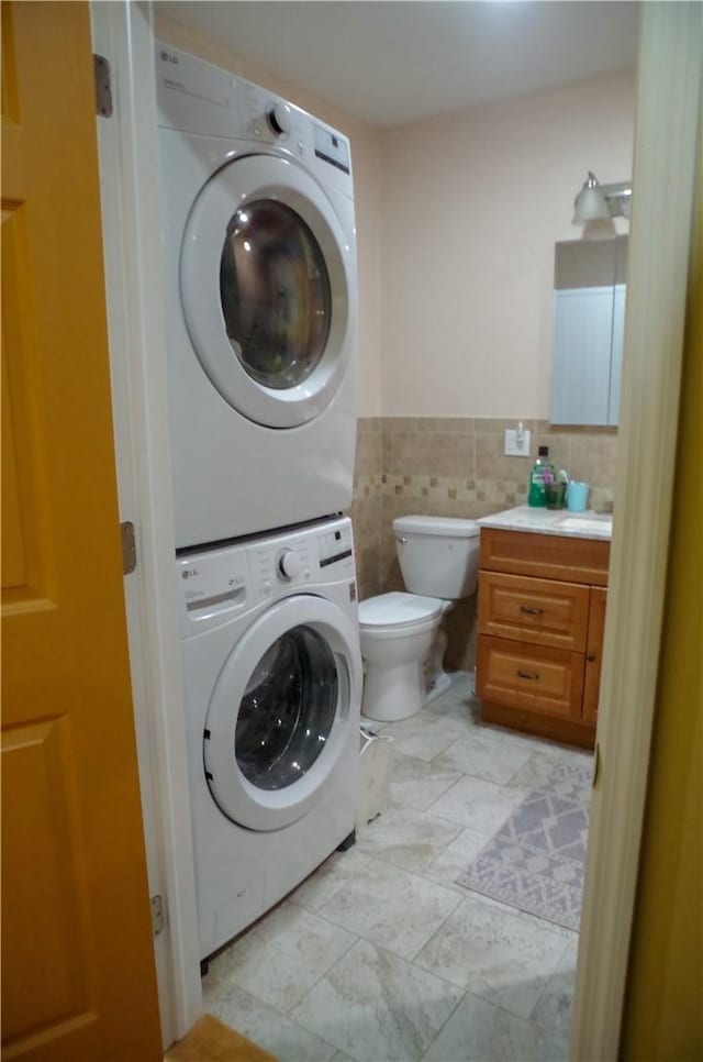 laundry room with stacked washer / dryer, light tile patterned floors, and tile walls