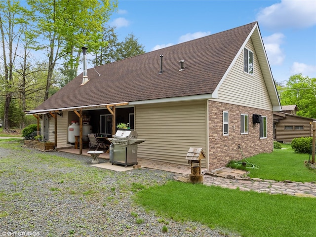 back of house with a shingled roof, a yard, a patio, and brick siding
