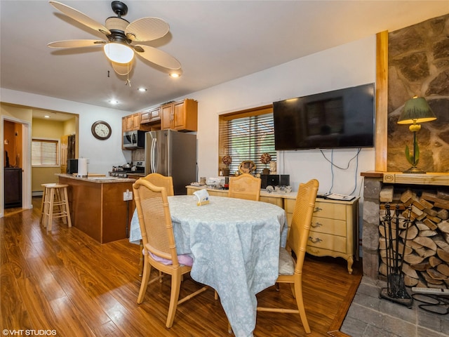 dining space with dark wood-style flooring, ceiling fan, an office area, and a stone fireplace