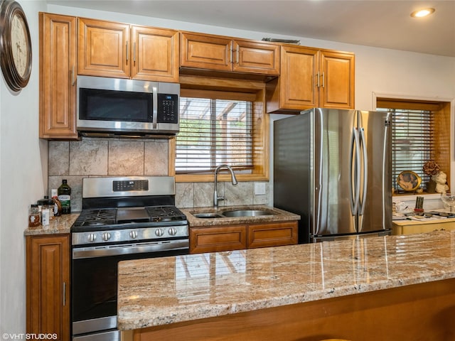 kitchen featuring appliances with stainless steel finishes, a sink, brown cabinets, light stone countertops, and recessed lighting