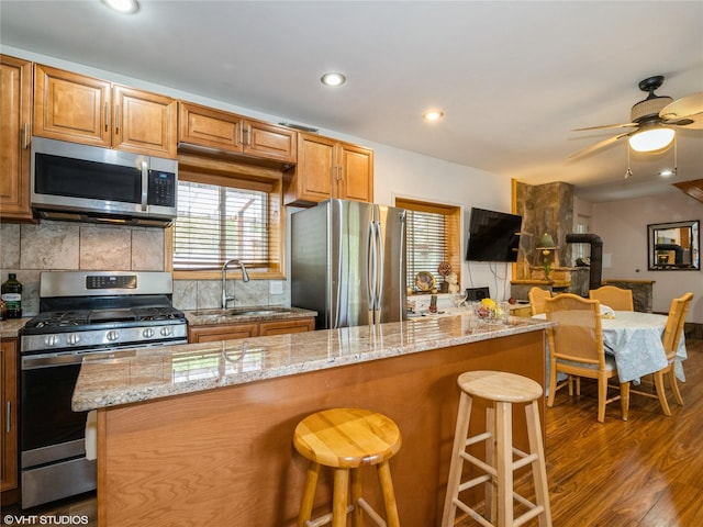 kitchen featuring appliances with stainless steel finishes, a sink, dark wood finished floors, a kitchen bar, and backsplash