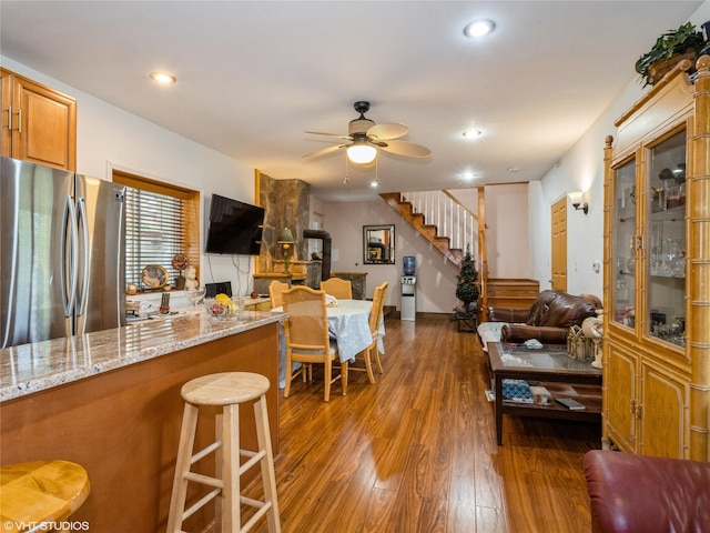 kitchen with freestanding refrigerator, dark wood finished floors, ceiling fan, brown cabinetry, and light stone counters