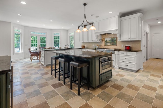 kitchen with a breakfast bar area, white cabinetry, stainless steel oven, and custom exhaust hood