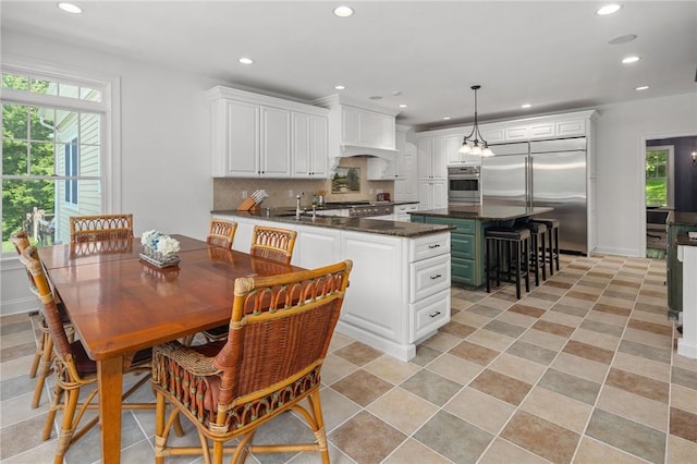 kitchen with kitchen peninsula, decorative backsplash, appliances with stainless steel finishes, decorative light fixtures, and white cabinetry